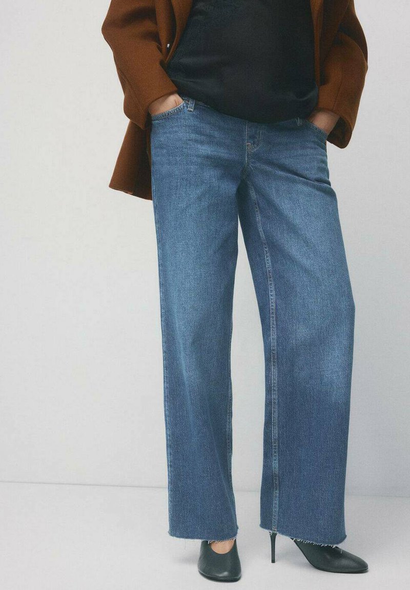 Szerokie niebieskie dżinsy z surowym wykończeniem nogawek, z wysokim stanem i przednimi kieszeniami, zestawione z czarnymi butami na obcasie i ciemną bluzką.