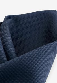 Námořnická modrá texturovaná tkanina s jemným diamantovým vzorem, složená pod úhly, které ukazují její hladký povrch a ohebné vlastnosti.
