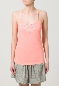 Koraalkleurige tanktop met kantdetail bij de buste, gemaakt van een zachte stof; gecombineerd met een gemusterde, geplooide rok in lichte kleuren.