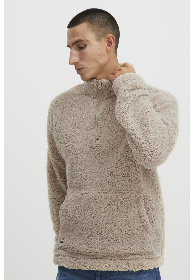 Beige fleece trøje med høj krave og halvlynlås. Har en blød, struktureret overflade og en forlommelomme. Afslappet pasform, perfekt til lag-på-lag.