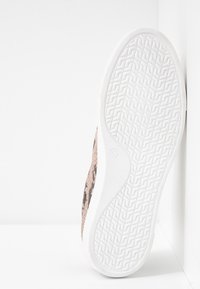 Baskets avec une tige beige à motif, en tissu texturé, et une semelle en caoutchouc blanc avec un motif en zigzag. Taille indiquée comme 37.