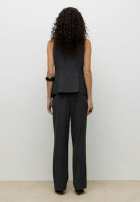 Czarny top bez rękawów o fasonie peplum, zestawiony z pasującymi, wysokim stanem i szerokimi nogawkami spodniami. Gładka tkanina z minimalnymi detalami.