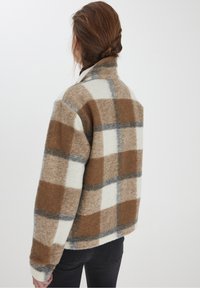 Hnědo-krémová károvaná fleecová bunda s šedými akcenty, vysokým límcem a volným střihem, strukturovanou látkou a dlouhými rukávy.