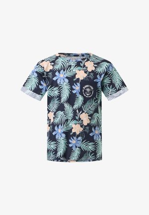 Garçon portant un T-shirt bleu marine à imprimé floral, un jean bleu, des baskets blanches, tenant des lunettes de soleil jaunes, regardant sur le côté sur un fond uni.