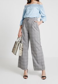 Jasnoniebieska bluzka odsłaniająca ramiona, szare spodnie w szerokie nogawki w szarą kratę oraz beżowa torebka z motywem węża na dwa uchwyty. Czarne sandały na paski.