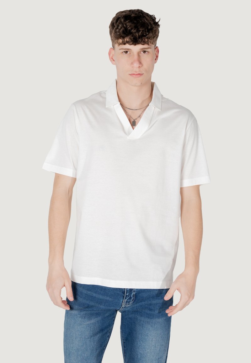 Polo shirt bianco in cotone a maniche corte con scollo a V, caratterizzato da una vestibilità comoda e una texture liscia, indossato con jeans blu.