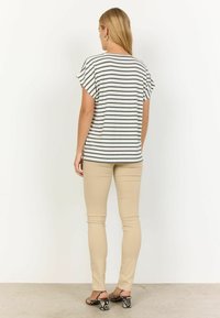 Stribet, kortærmet top i hvid og mørkegrå, parret med beige tætsiddende bukser og sko med slangeskindsprint. Visning fra ryggen.