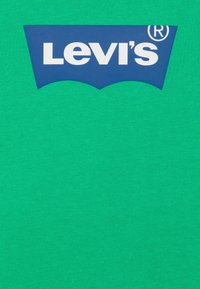 Maglietta in cotone verde con un grande logo Levi’s blu con testo bianco, inserito in una distintiva forma curva.