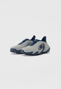 Lys grå slip-on sko med marineblå accenter, teksturert gummisåle og avrundet design. Har et side-logo og polstret øverste lag.