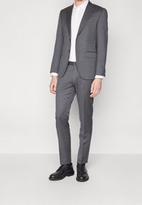Grå kostym med slim fit, med en slagen krage och tvåknäppning. Kombinerad med en vit skjorta och svarta dress skor.