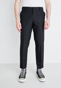 Musthave püksid, millel on slim fit lõige, lapik esiosa ja kaks küljetaskut. Kandmisel mustad kõrge kontsaga tossud valgete talladega.