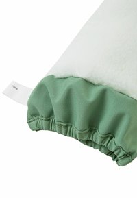 Grüner Stoff mit strukturierter Oberfläche, weißer Fleece-Überlagerung, unten mit eingefasstem Gummizug und Namensschild.