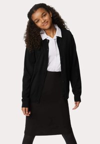 Czarny kardigan z zapięciem na guziki, noszony na białej koszuli z kołnierzykiem i czarnej spódnicy. Posiada ściągacze przy mankietach i u dołu oraz miękką fakturę.