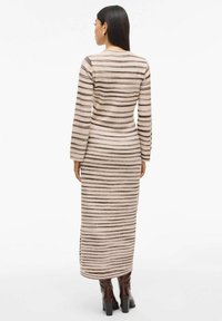 Lang, tettsittende kjole laget av myk stoff med horisontale brune striper på en lys bakgrunn. Den har lange ermer og rund hals.