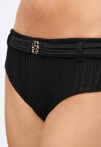 Μαύρο ριμπ ψηλόμεσο μαγιό κάτω μέρος με ταιριαστή ζώνη που διαθέτει μεταλλικό διπλό κούμπωμα B στη μέση και το επάνω μέρος των μηρών ενός ατόμου.