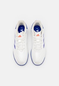 Zapatillas deportivas blancas con acentos azules y tres rayas rojas. Presentan un diseño de cordones, material sintético suave y suela texturizada.