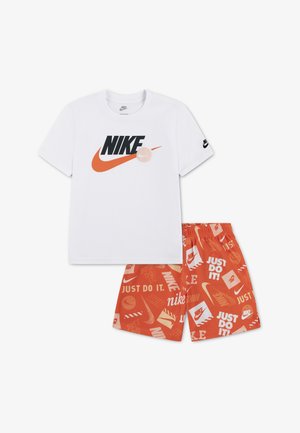 Camiseta blanca de Nike con un gran logo negro y naranja, combinada con pantalones cortos naranjas que llevan varios logos de Nike y el texto "Just Do It".