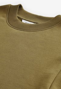 Sudadera verde oliva con un cuello redondo acanalado y textura de tela suave, con un dobladillo cosido ordenado y una etiqueta visible en el interior.