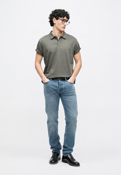 Polo gris à motif avec manches retroussées, associé à un jean bleu clair et des mocassins noirs. La tenue présente un style minimaliste.