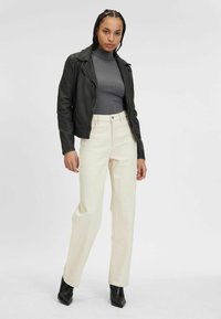 Giacca da motociclista in pelle nera, dolcevita a coste grigio, pantaloni larghi color crema e stivaletti neri alla caviglia. Design semplice e colori neutri.