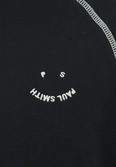 Svart tyg med en slät textur som har vit broderi av texten "PAUL SMITH" och en smiley-ansikte grafik.