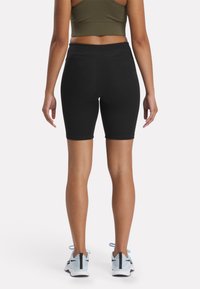 Shorts de ciclismo negros con una textura suave, cinturilla alta, combinados con zapatillas deportivas azul claro que presentan un diseño de malla y acentos negros.