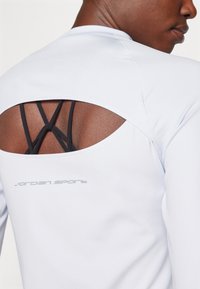 Hvit treningsskjorte med en unik utskåret bakside, svart stroppedetalj og et reflekterende "Jordan Sport"-logo nederst på ryggen.