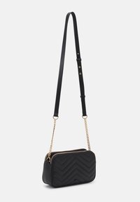 Černá crossbody taška s prošívaným chevron vzorem, zlatým řetízkem a koženými popruhy, se zipovým uzávěrem, obdélníkového tvaru a hladkou texturou.