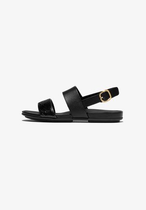Black sandal featuring a glossy leather upper with a textured sequin strap, adjustable buckle, and a flat rubber sole.