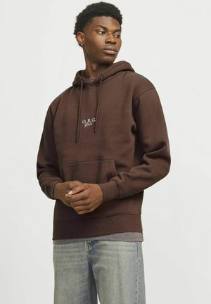 Haut en coton marron avec cordon de serrage réglable, poche kangourou à l'avant et logo brodé. Le modèle porte un jean bleu clair.