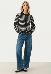 Striped cardigan with navy and cream colors, round neckline, full buttons, textured fabric, paired with high-waisted blue jeans and black flats.