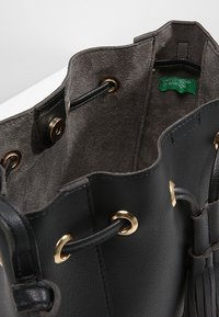 Svart läderhandväska med mjuk textur, guldfärgad hårdvara och en inredning av tyg. Har dragsnöre-öppning och varumärkesetikett synlig.