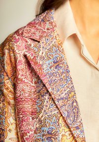 Blazer colorato a motivi con intricati disegni floreali nelle tonalità di rosa, blu e oro. Il tessuto ha un aspetto tessuto e testurizzato.