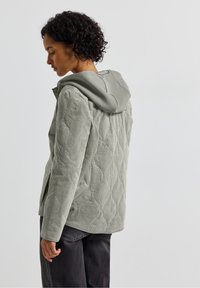 Quilted green jacket with a hood, featuring a textured fabric and a fitted silhouette. The back displays a diamond pattern for added detail.