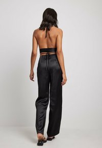 Haut halter en satin noir sans dos associé à un pantalon large taille haute en satin noir. Texture lisse, lien réglable à la taille.