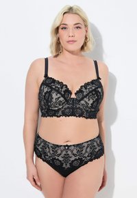 Zwarte kanten bralette met scalloped rand, voorzien van bloemmotieven en verstelbare bandjes. Gecombineerd met bijpassende hoge kanten slipjes.