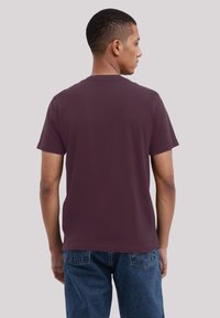 Maroon cotton t-shirt with short sleeves, classic crew neck, and plain design. Worn with blue denim shorts. Back view shows fabric drape.