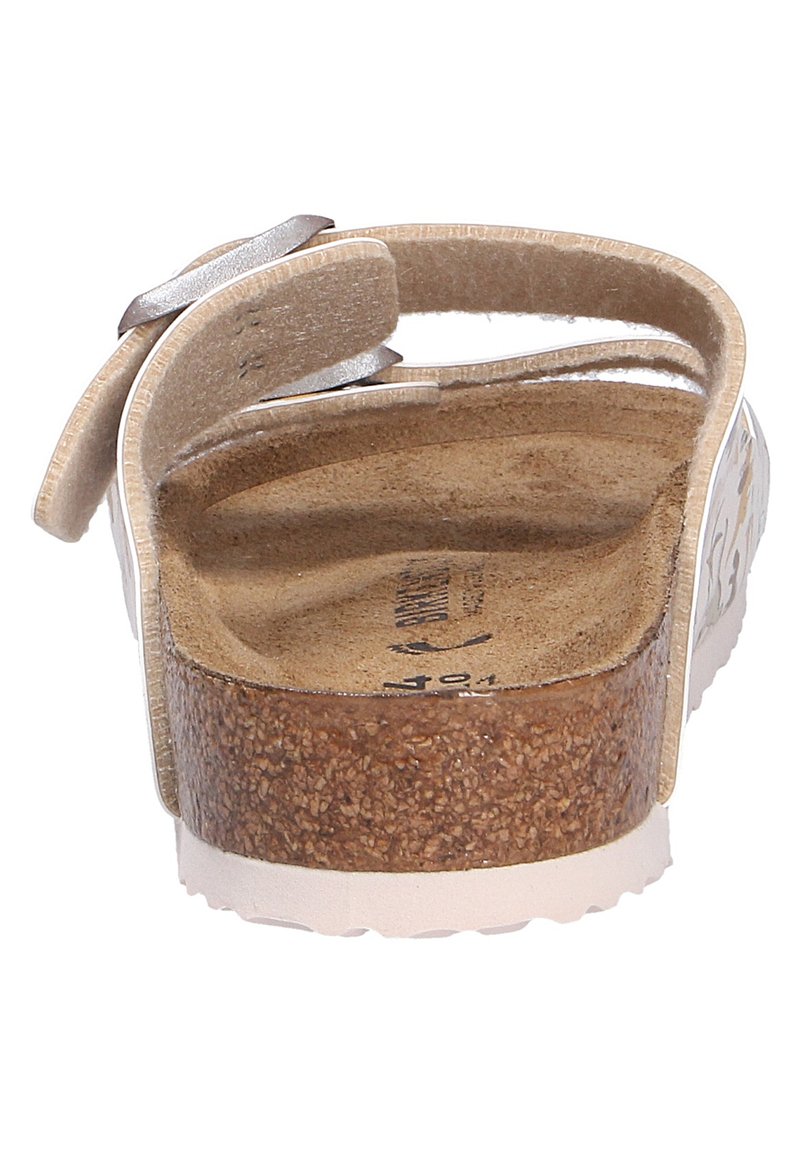 Sandales blanches avec une semelle en liège et une sangle argentée brillante, présentant une semelle intérieure texturée. Design à dos ouvert avec une semelle surélevée.