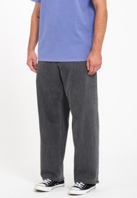 Grijze denim broek met een losse pasvorm, met een klassiek vijf-pocket ontwerp en contrasterende stitching, vergezeld van zwarte canvas sneakers.