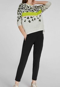 Suéter gris claro con estampado de leopardo negro y amarillo, combinado con pantalones negros ajustados. Tejido cómodo con cintura ajustable.