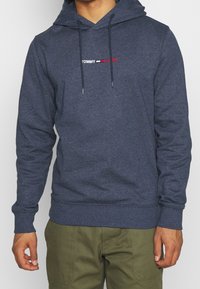 Marinblå huvtröja med en frontlogotyp i vitt och rött. Har dragsko i huvan samt ribbade muddar och nederkant.