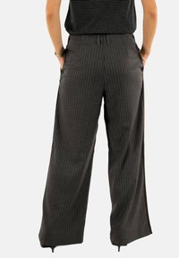 Pantalons à jambes larges en tissu noir à rayures grises avec une taille élastique et des poches latérales. Présente une coupe décontractée et un design à ourlet ouvert.