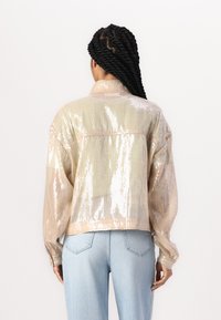 Cropped, collared jacket made from sequined fabric in beige and gold tones. Features long sleeves and a loose fit. Back view.