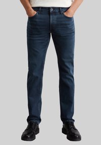 Donkerblauwe jeans met een rechte pasvorm, voorzien van voorzakken, een ritsgulp en een enkele knoopsluiting. Draag ze met zwarte schoenen.