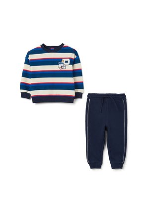 Sweatshirt rayé à manches longues en bleu, crème et rouge avec un détail graphique, associé à un pantalon de jogging navy avec des bandes blanches sur les côtés.