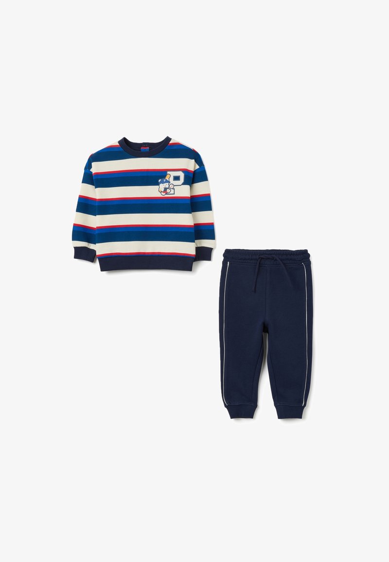 Felpa a maniche lunghe a righe in blu, crema e rosso con un dettaglio grafico, abbinata a pantaloni della tuta blu scuro con strisce bianche laterali.