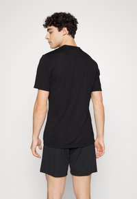 Chemise noire à manches courtes en tissu lisse, avec un col rond et une coupe ample, accompagnée de shorts de sport noirs.