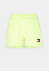 Neon žluté bavlněné šortky s elastickým pasem a šňůrkou na stažení. Na levé straně je nášivka s logem. Hladký povrch.