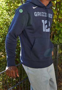 Felpa Nike blu navy con tasca frontale, testo "GRIZZLIES" e numero "12" in azzurro chiaro. Materiale morbido simile al pile con cappuccio regolabile.