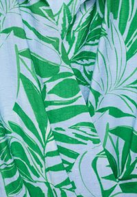 Textil cu un model de frunze verde și alb, pe un fundal de un albastru deschis. Materialul pare ușor și are o suprafață ușor texturată.